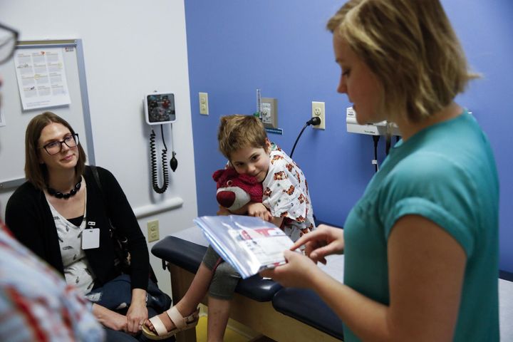 Photo of a mother, a little child with a red teddy bear, and a healthcare worker in an exam room